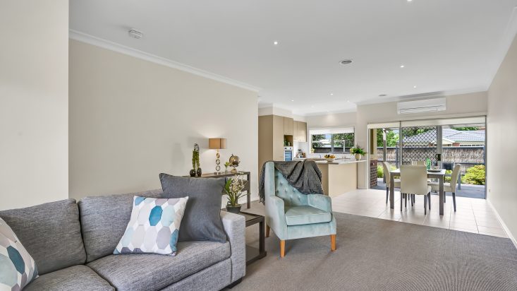 Lounge room with grey couch and light blue armchair, kitchen and dining room in background