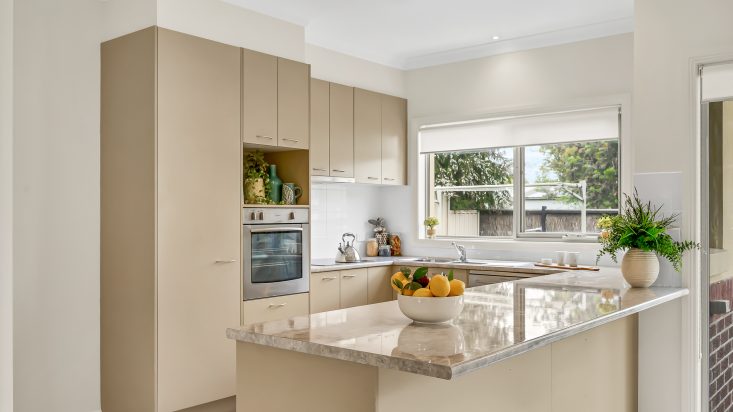 Beige U-shaped kitchen in unit at Corpus Christi Retirement Village, bench overhangs to use as a breakfast bar, fruit bowl on bench