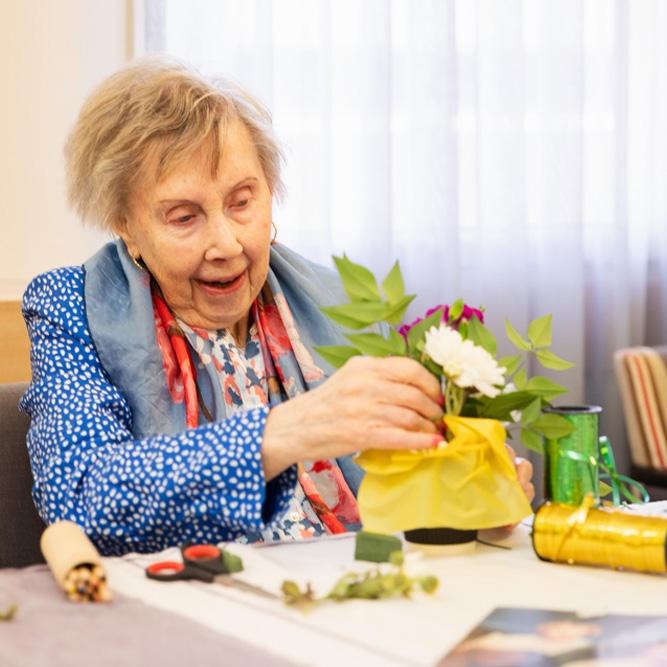 An older lady arranging flowers sitting at a table