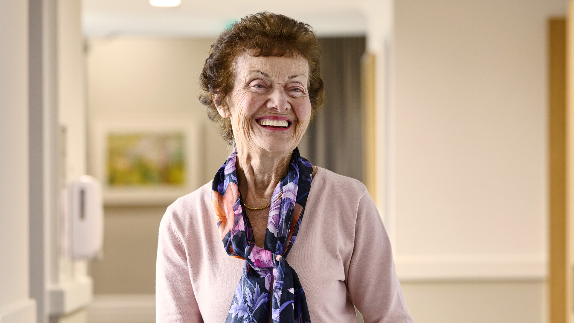 An older woman smiling as she walks down a hallway