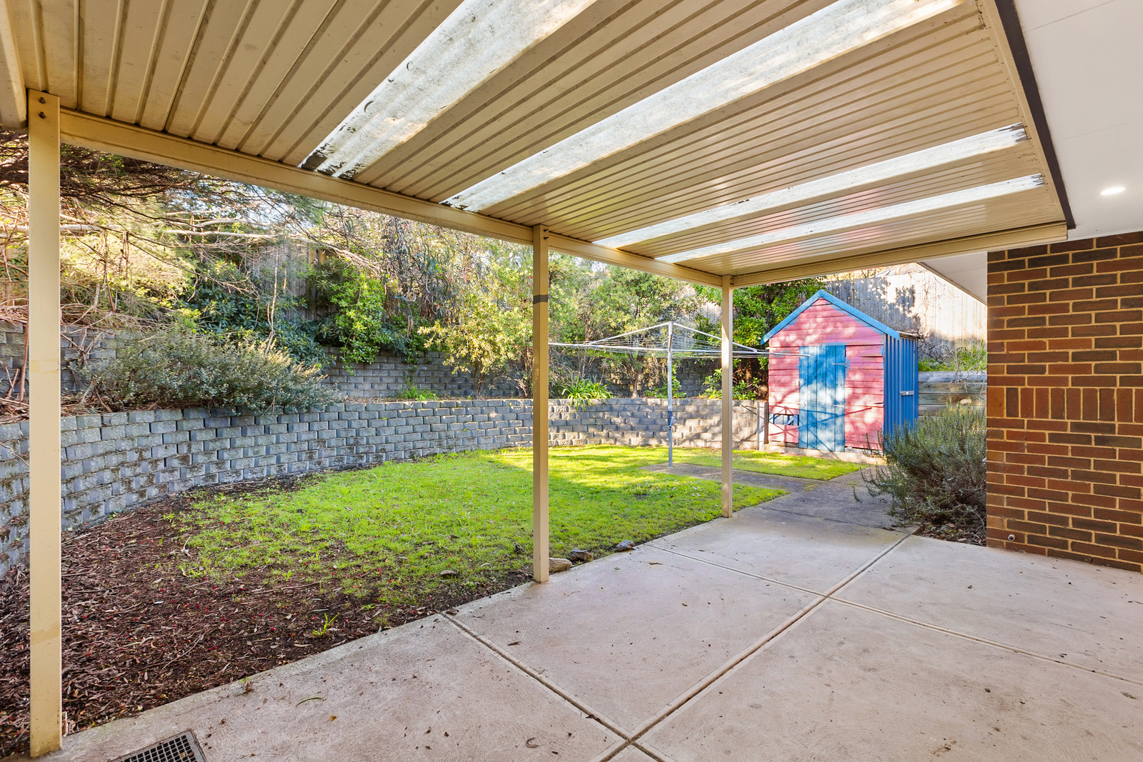 A backyard with a patio undercover. A red and blue cubby house sits in the far corner.