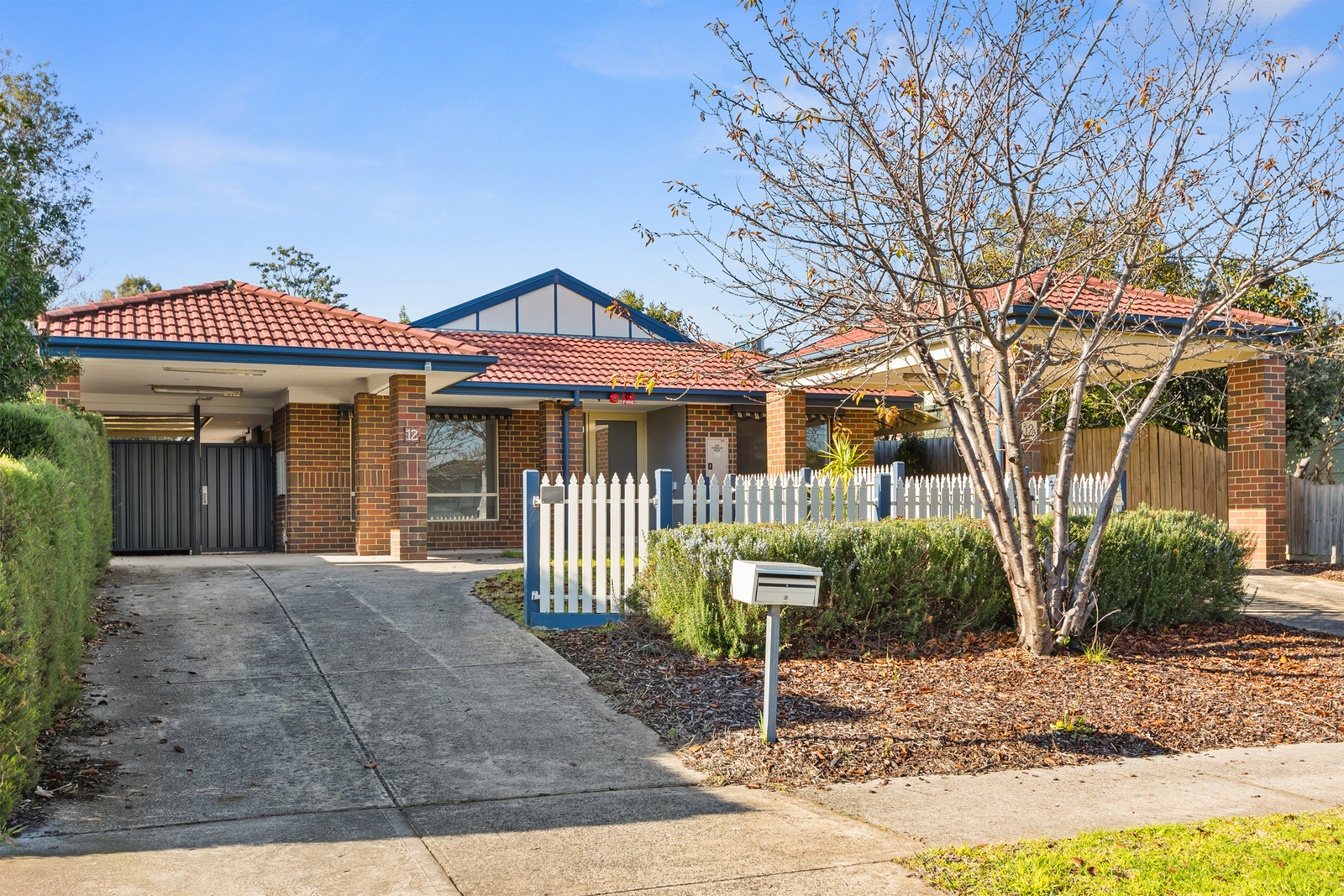 A house with a roof tiled in red tiles and a concreate driveway with a blue and white picket fence.