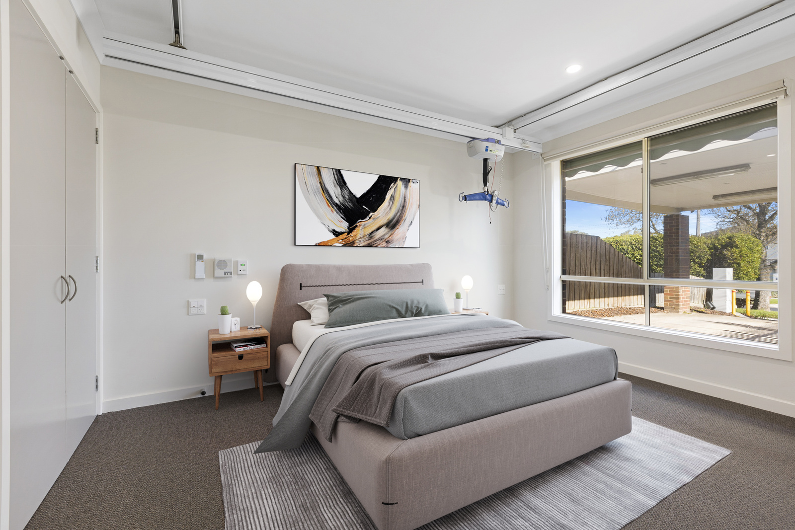 A bedroom with a large window and ceiling track rails.