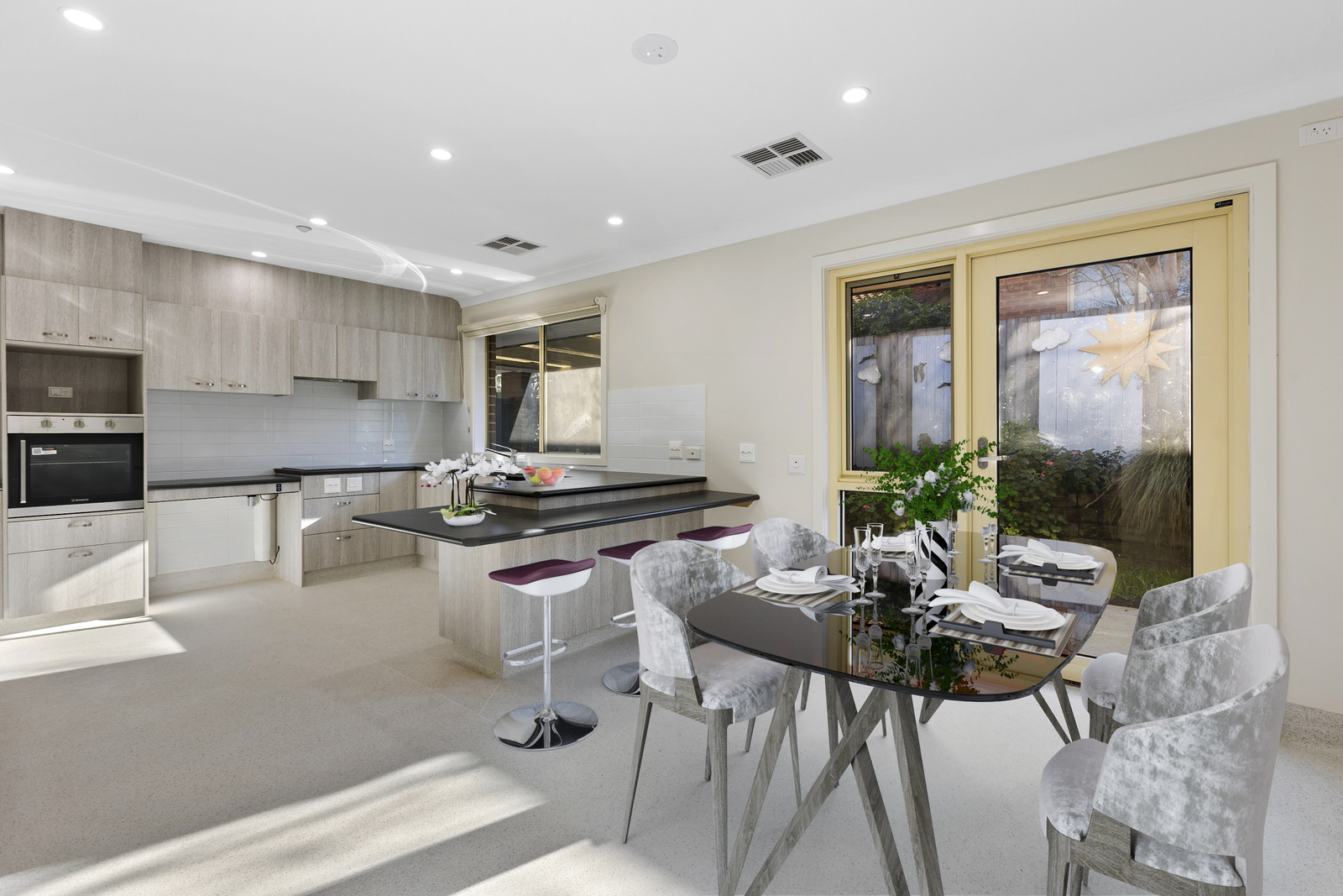 A modern kitchen with stools at the bench as well as a kitchen table that is set with dinner ware.