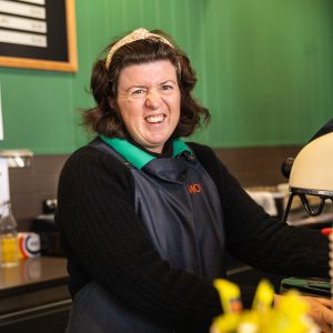 A woman working in a coffee shop, standing at the commercial coffee machine