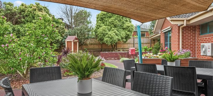 Berwick Aged Care outdoor table and chairs underneath a canvas covering. Plants and trees in the background.