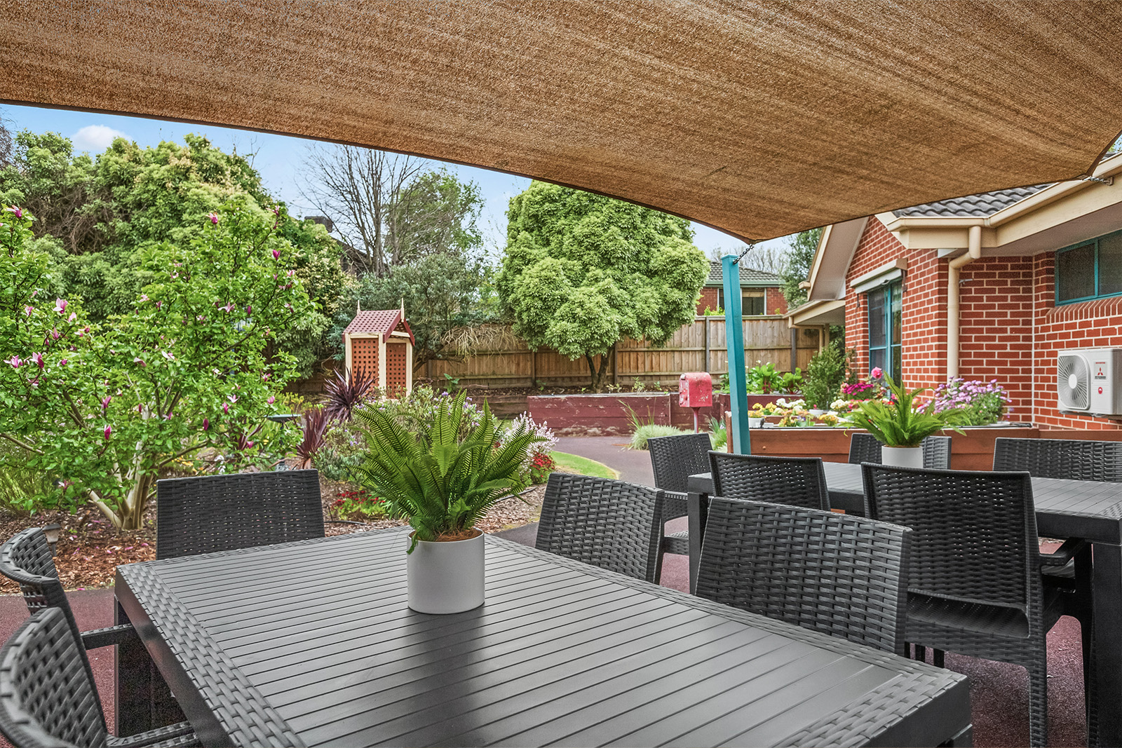 Outdoor table and chairs underneath a canvas covering. Plants and trees in the background.