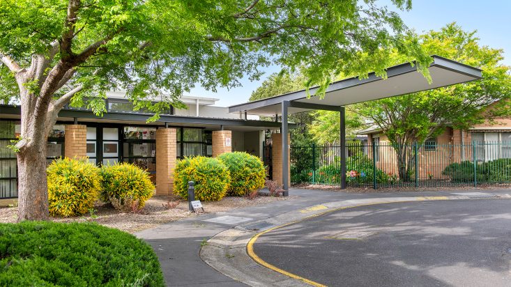 A driveway that leads to the entrance of the aged care residence surrounded by green trees.