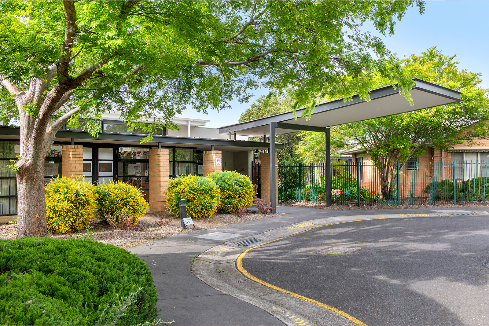 A driveway that leads to the entrance of the aged care residence surrounded by green trees.