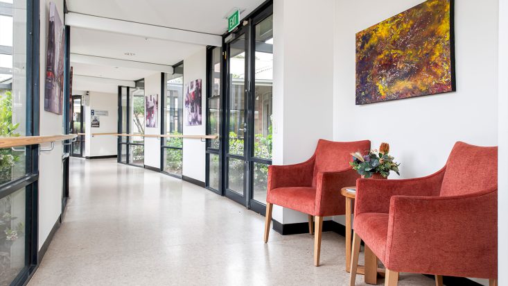 A bright hallway with large windows and two red arm chairs.