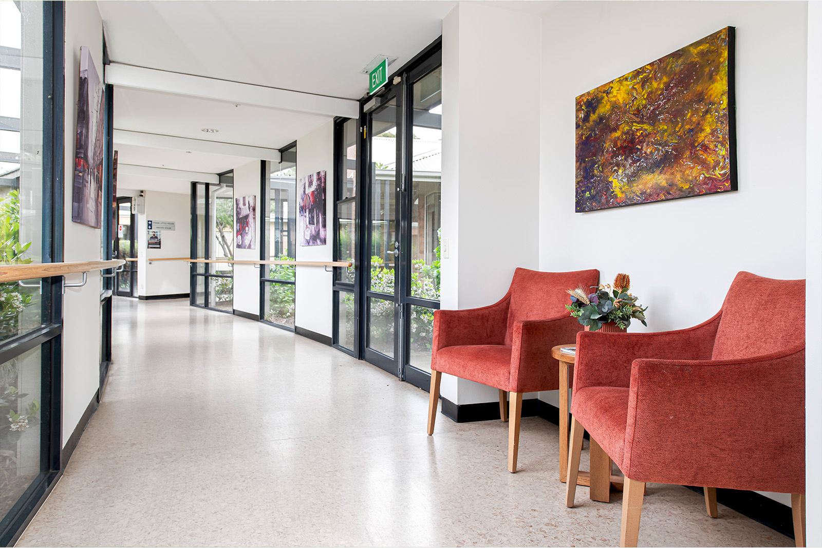 A bright hallway with large windows and two red arm chairs.