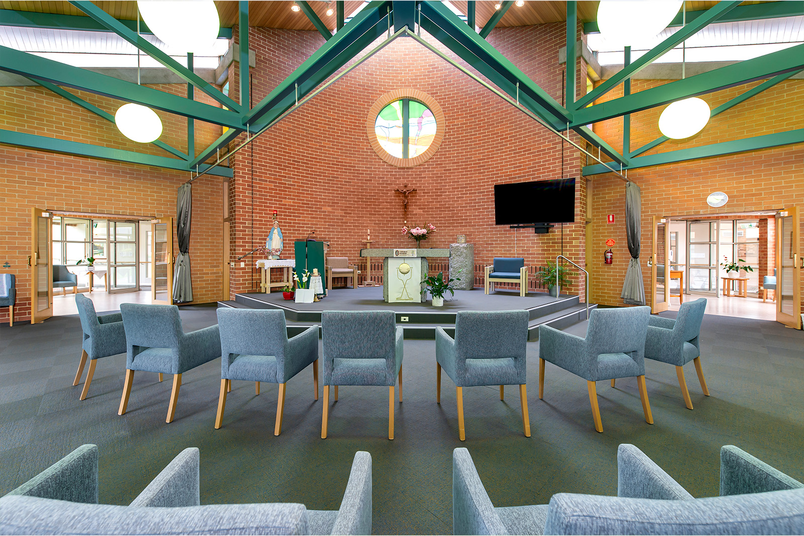 A chapel with green beams across the ceiling. Small armchairs are arranged to face the altar.