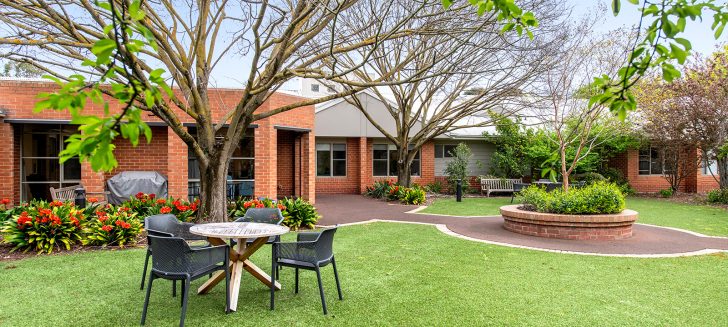 A table and chairs set on the grass near a redbrick building.