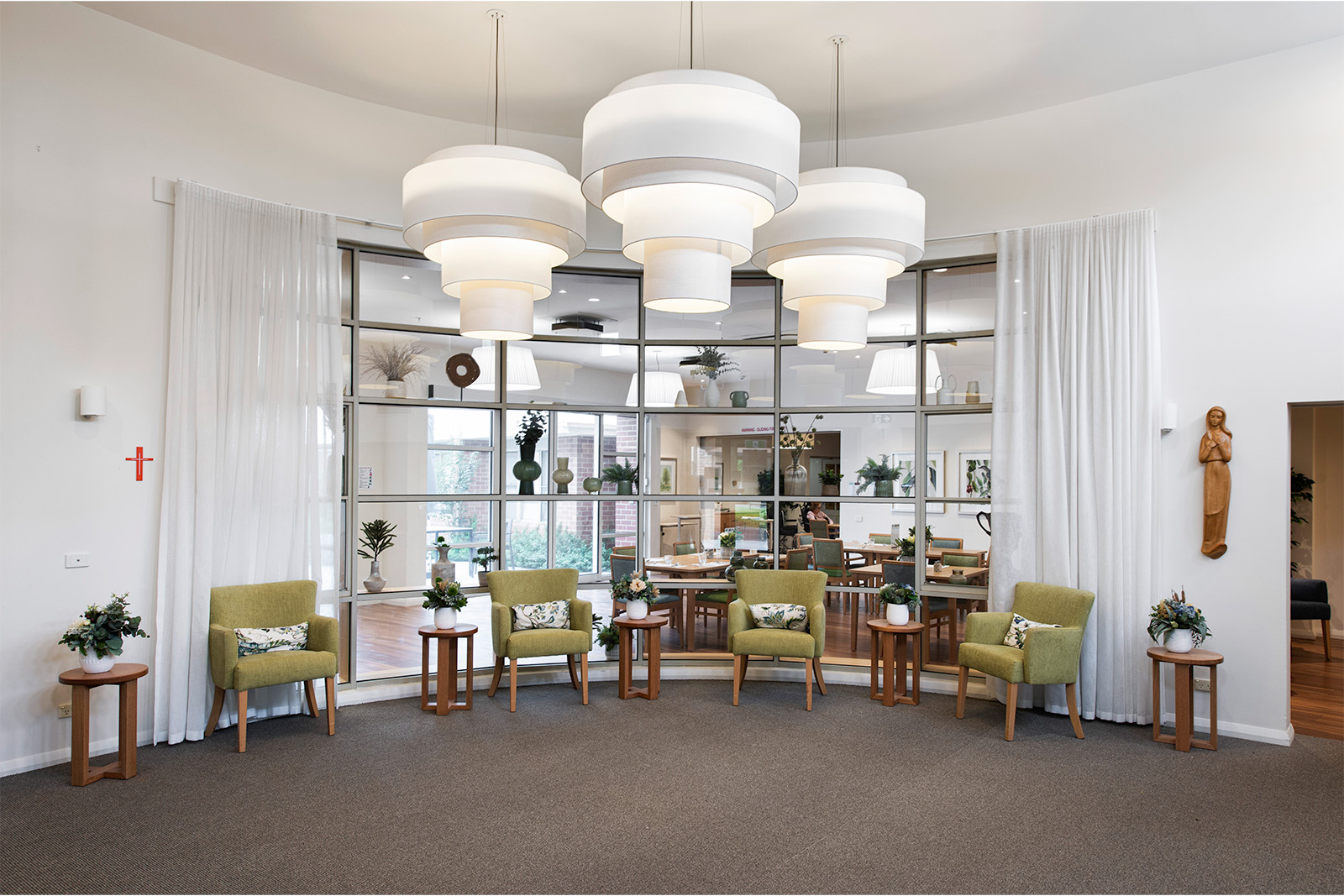 A living space with green armchairs along the window which looks into the dining room. A large light feature hangs in the centre of the room.