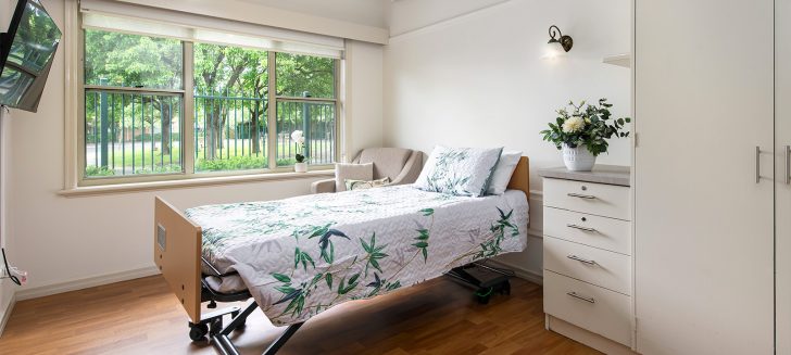 A bedroom with a large window and an armchair in the corner beside the bed.