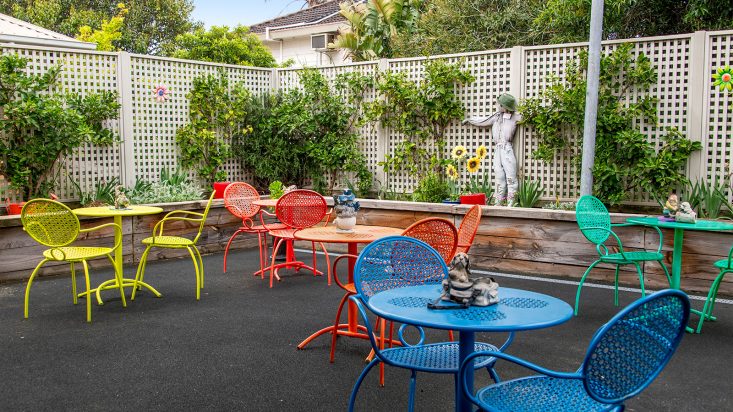 A courtyard filled with metal chairs and tables, all different colours in yellow, red, green and blue.