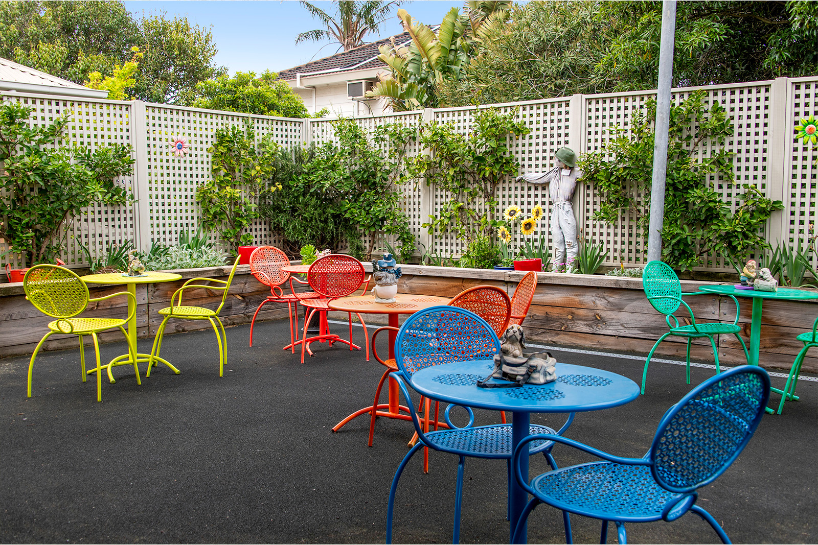 A courtyard filled with metal chairs and tables, all different colours in yellow, red, green and blue.