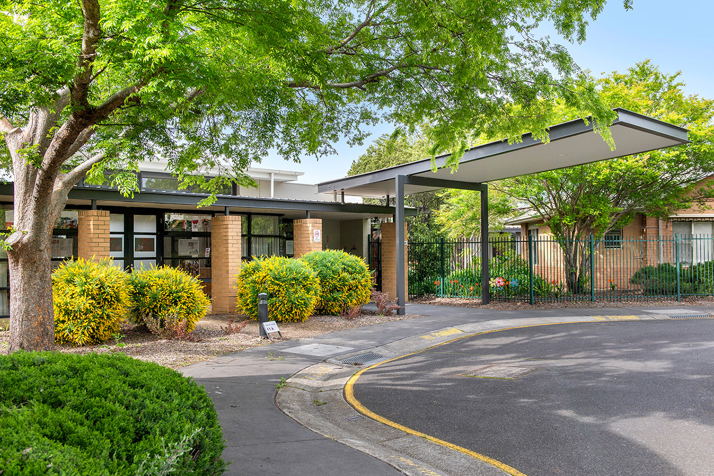 A driveway that leads to the entrance of the aged care residence surrounded by green trees.