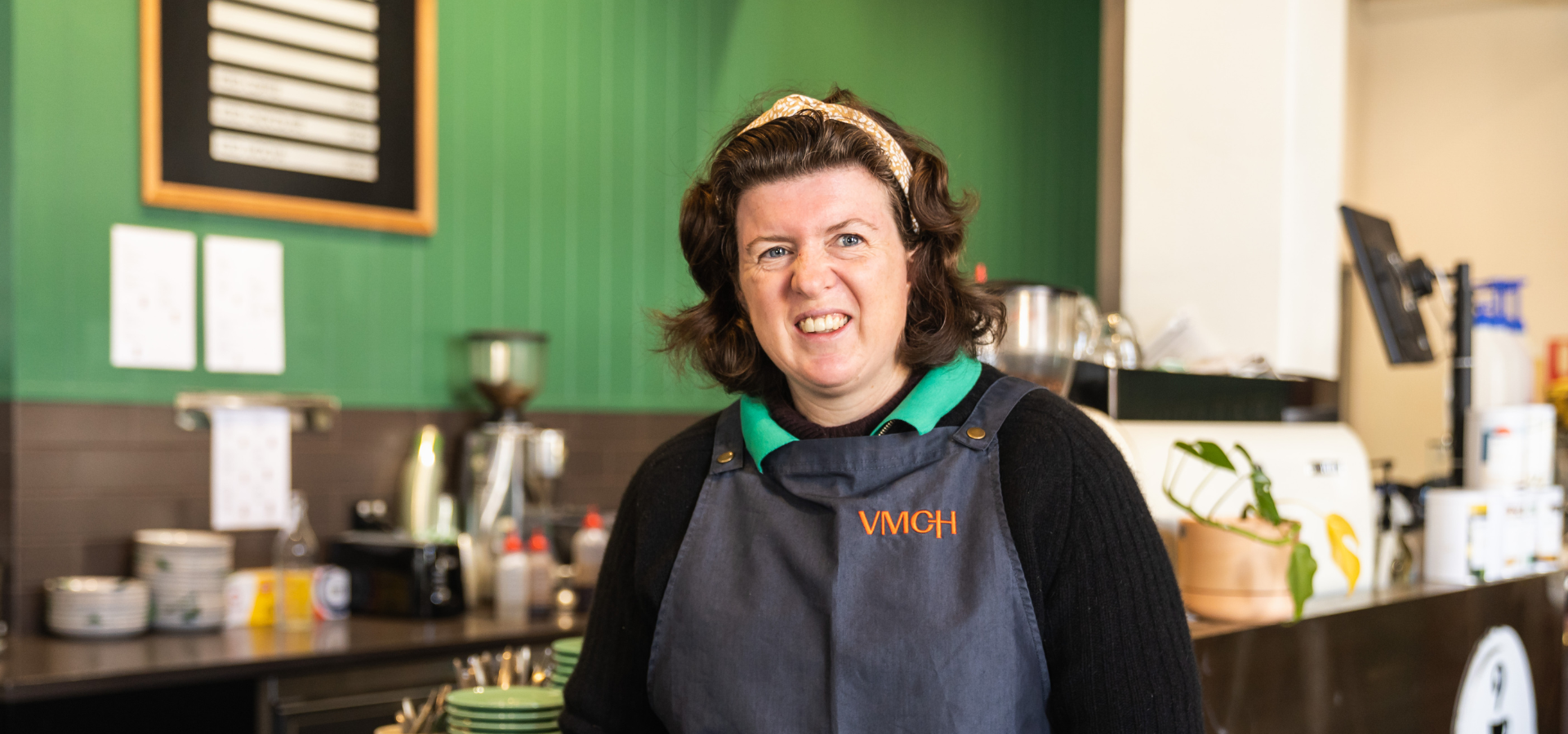 A woman standing in a cafe smiles at the camera