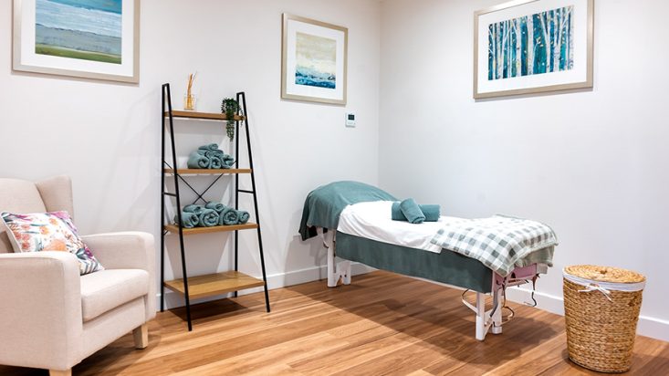 A massage bed next to a shelf full of towels.