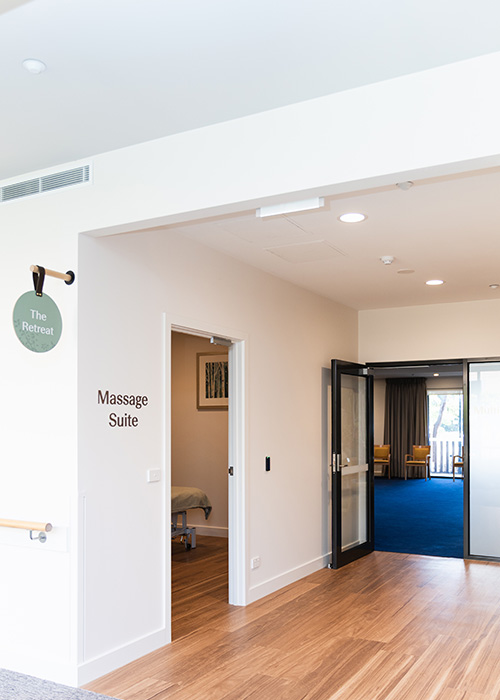 Entrance to a massage suite in a wellness center with wooden flooring and a blue-carpeted room in the background.