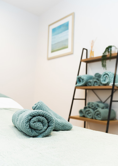 A neatly made bed with folded towels beside a shelf displaying a framed picture.