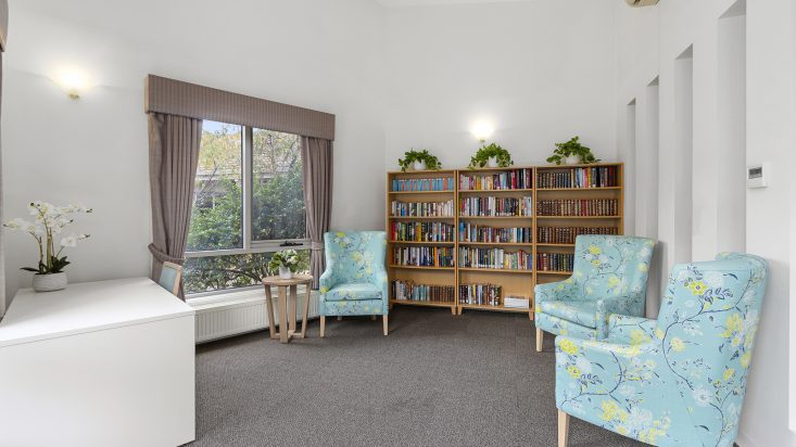 A living room with armchairs and bookshelves at St Bernadette's Aged Care.