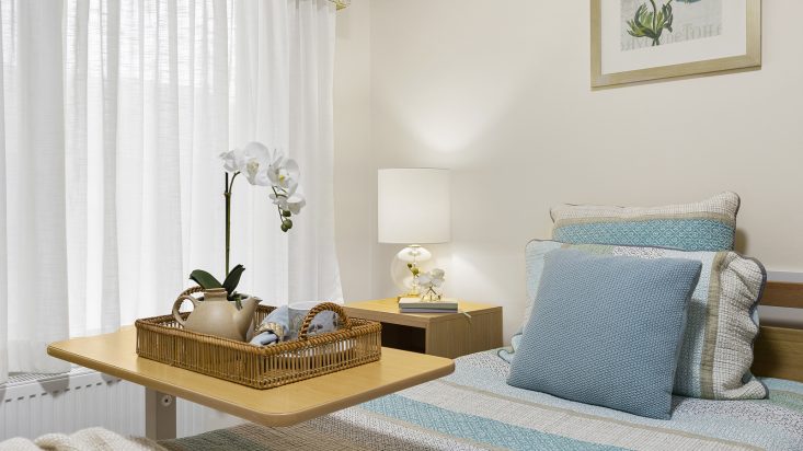 A bedroom with a curtained window and tea set on a tray on a table at St Bernadette's Aged Care.