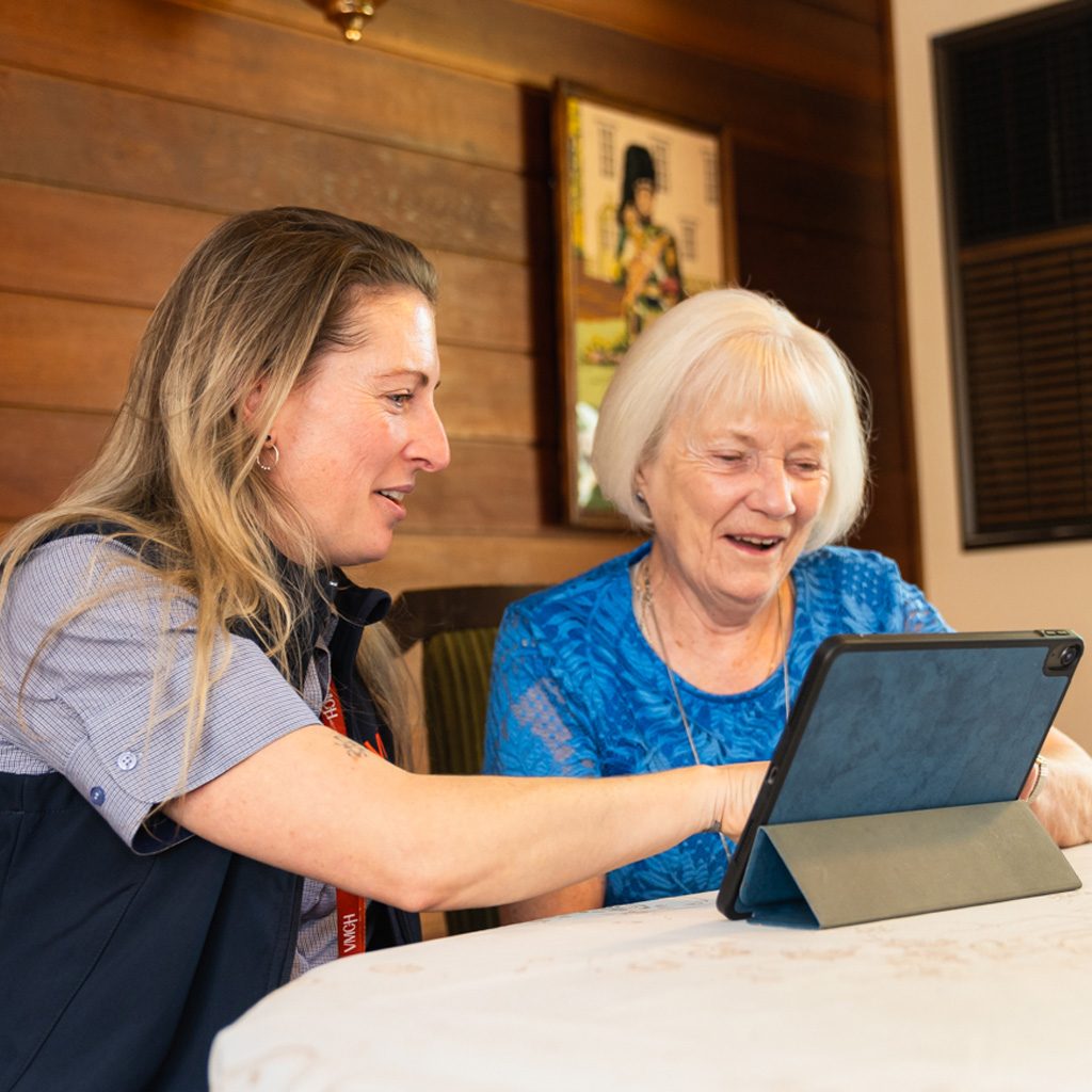 A support worker helping an older woman with an iPad.