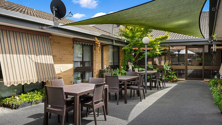 An enclosed outdoor space with multiple tables and chairs underneath a patio shade.