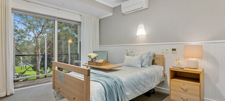 A bedroom with large windows and a soft blue quilt set.