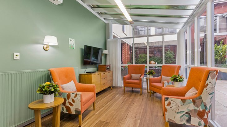 A bright green living space filled with windows and orange armchairs.