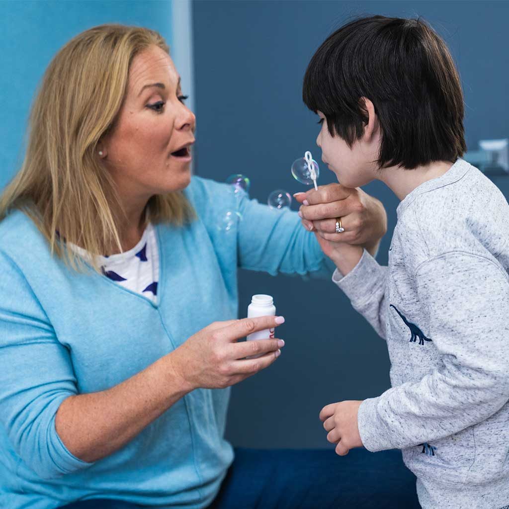 A young boy blowing bubbles with the help of his carer