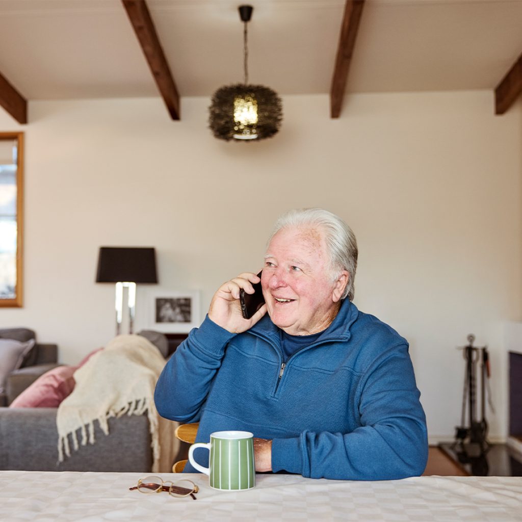 An older man on the phone, sitting at the dinner table.