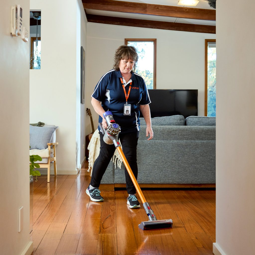 A woman using a stick vacuum to clean a hardwood floor.