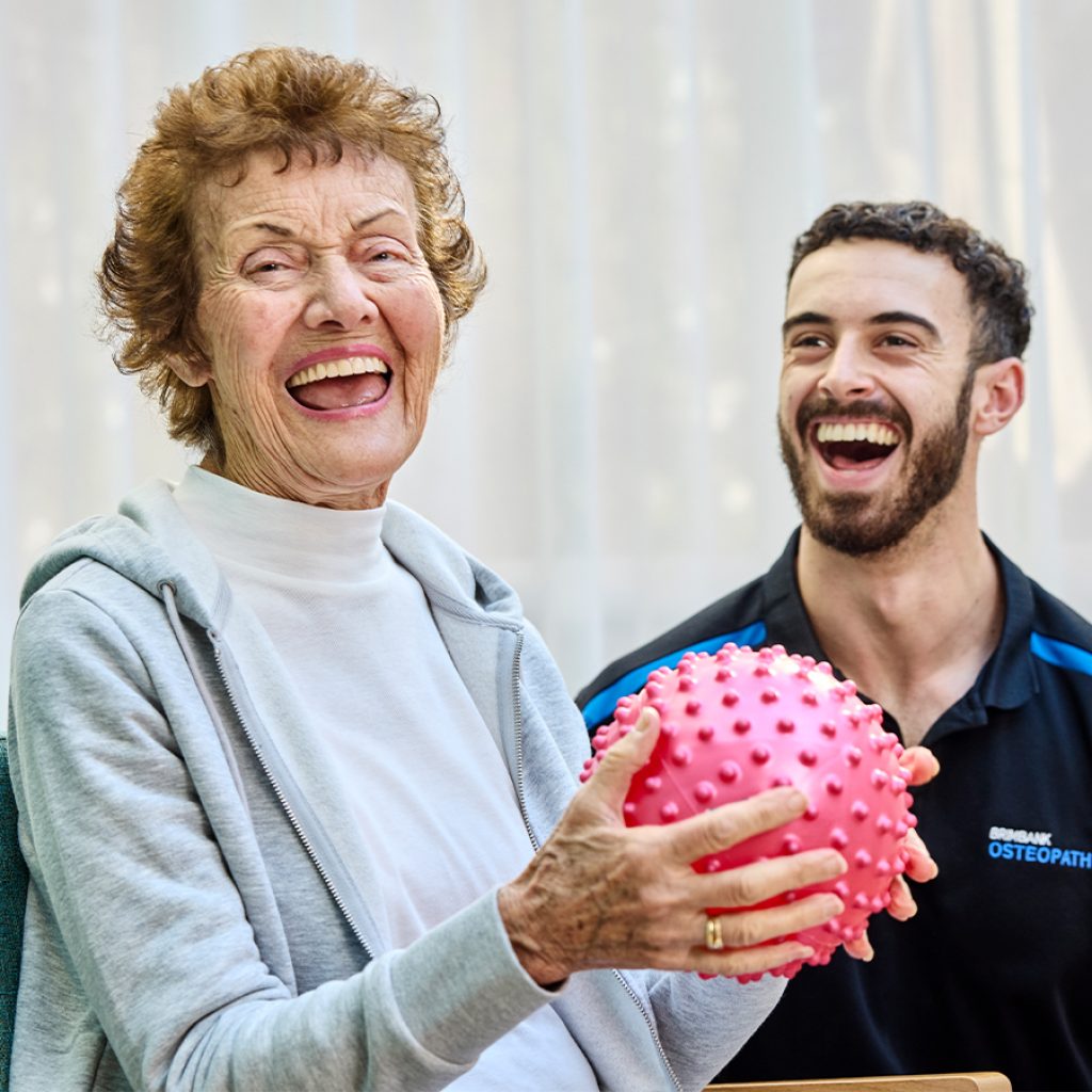 A woman laughing with her physio while holding a spiky ball.