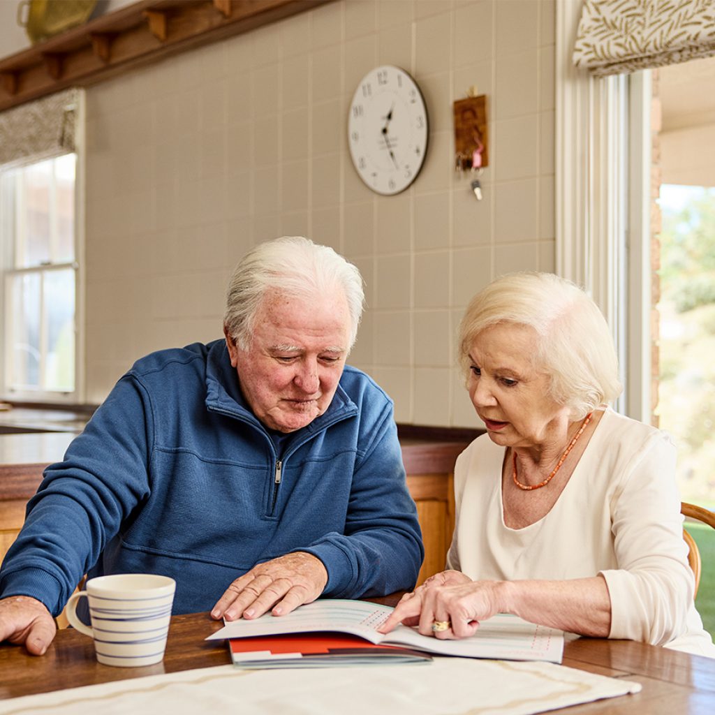 An older couple looking at Assistive Technology and Home Modifications (AT-HM) Scheme paper work in the kitchen.
