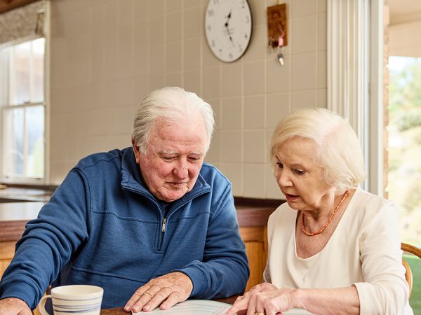 An older couple looking at Assistive Technology and Home Modifications (AT-HM) Scheme paper work in the kitchen.