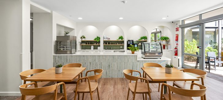 A light-filled cafe with white walls and a blue bench at Corpus Christi Clayton Aged Care.