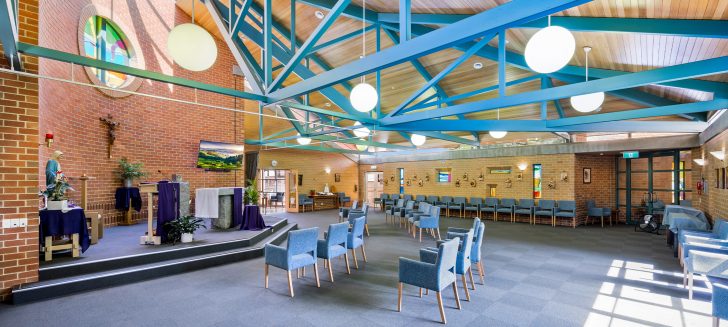A spacious chapel with bright blue framework in the ceiling and a colourful mosaic above the altar.