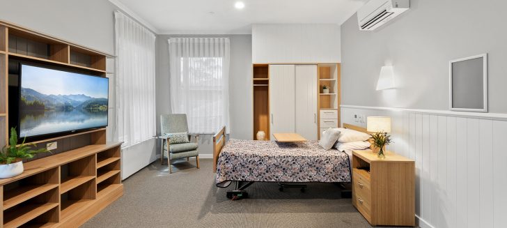A bedroom with large windows and a soft pink quilt set.