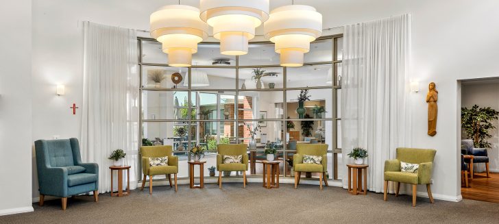 Green armchairs line a wall of windows that separate two rooms.