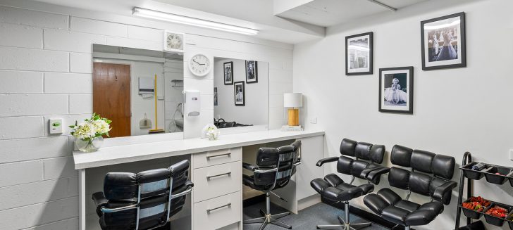 A salon with two armchairs in front of a mirror and framed pictures of old Hollywood stars on the wall.