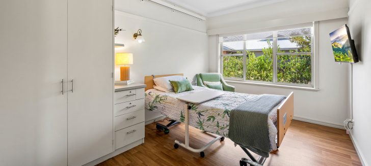 A bedroom with greenery outside the windows and a bright lamp on.
