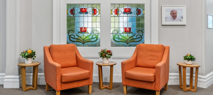 Two vermillion armchairs in front of a glass mosaic window.