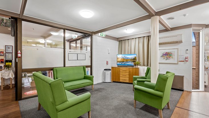 A green couches sit facing a television with a window behind it.