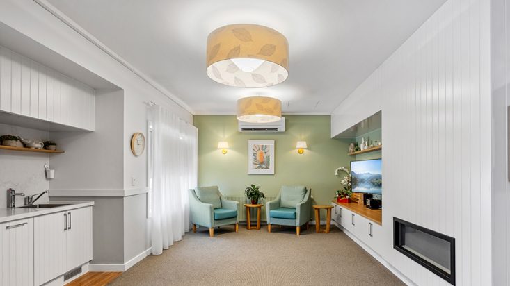 A living space with a green feature wall and blue armchairs by a television.