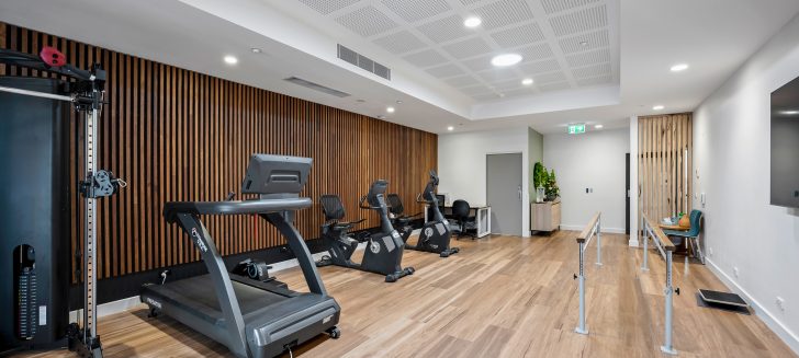 A gym with a treadmill, multiple exercise bike and a lovely wooden feature wall.