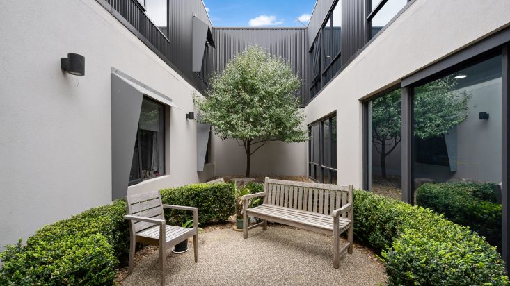 A small, enclosed garden surrounded by walls with bushes and benches.