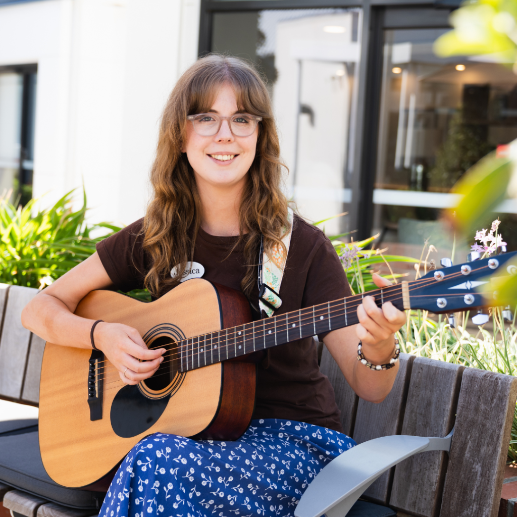 A woman sits holding a guitar